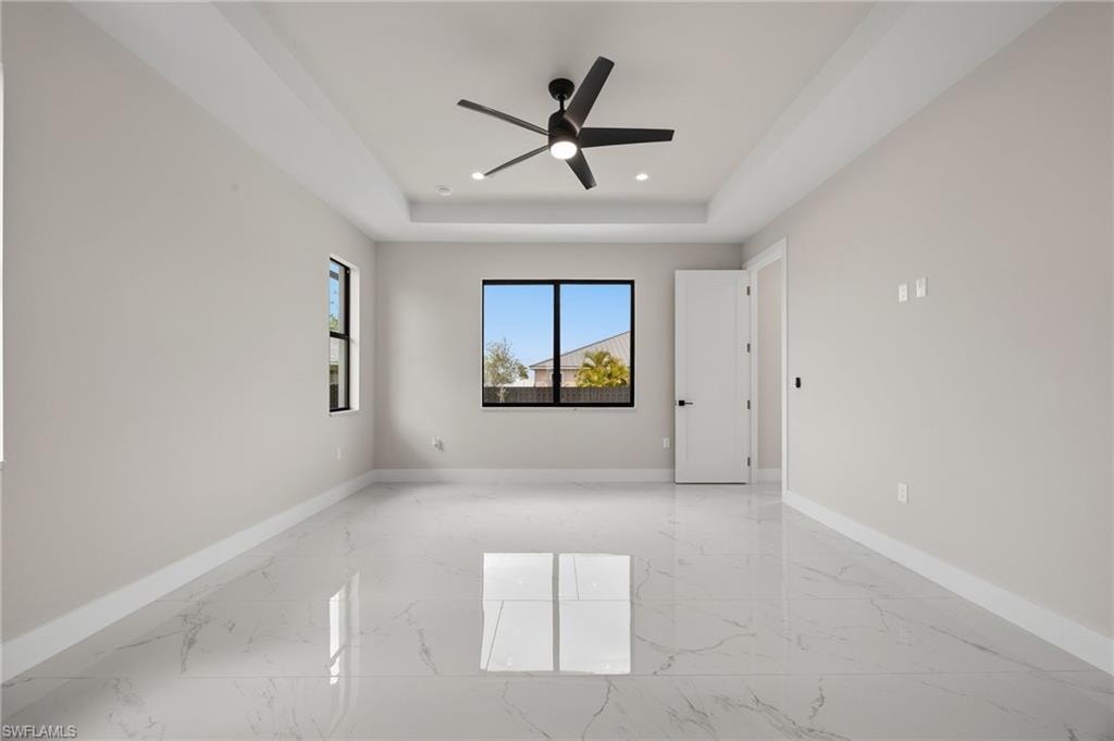 Empty room featuring ceiling fan, light marble finish flooring, a raised ceiling, and recessed lighting