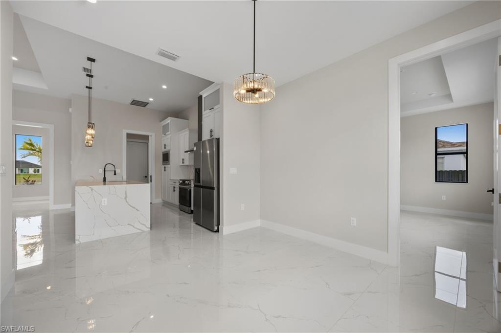 Kitchen with plenty of natural light, a tray ceiling, stainless steel appliances, white cabinetry, and suspended lighting