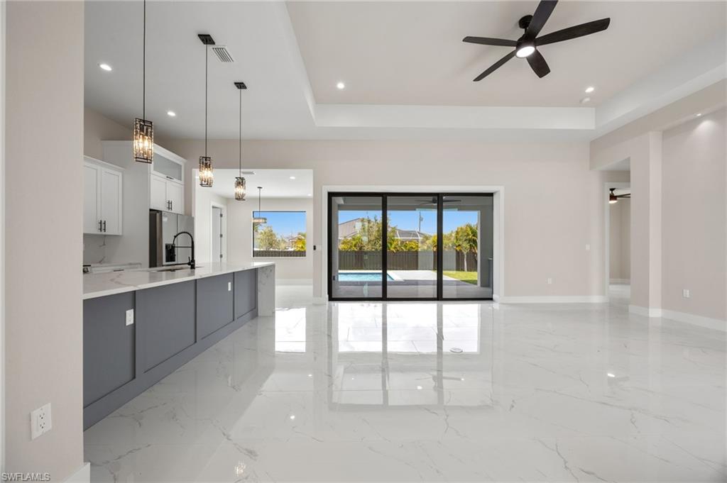 Kitchen featuring a tray ceiling, light stone countertops, a ceiling fan, pendant lighting, and stainless steel fridge with ice dispenser