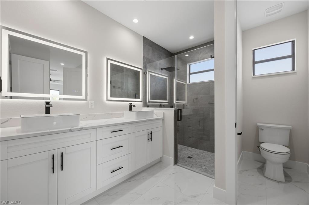 Bathroom with double vanity, a stall shower, light marble finish flooring, and recessed lighting