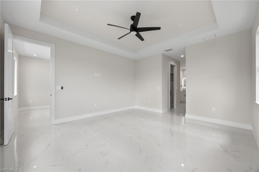 Unfurnished room featuring a tray ceiling, ceiling fan, recessed lighting, and light marble finish floors