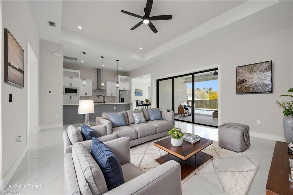 Living room featuring ceiling fan, a tray ceiling, recessed lighting, and light marble finish flooring