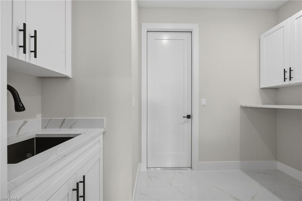Laundry area featuring cabinet space and light marble finish floors
