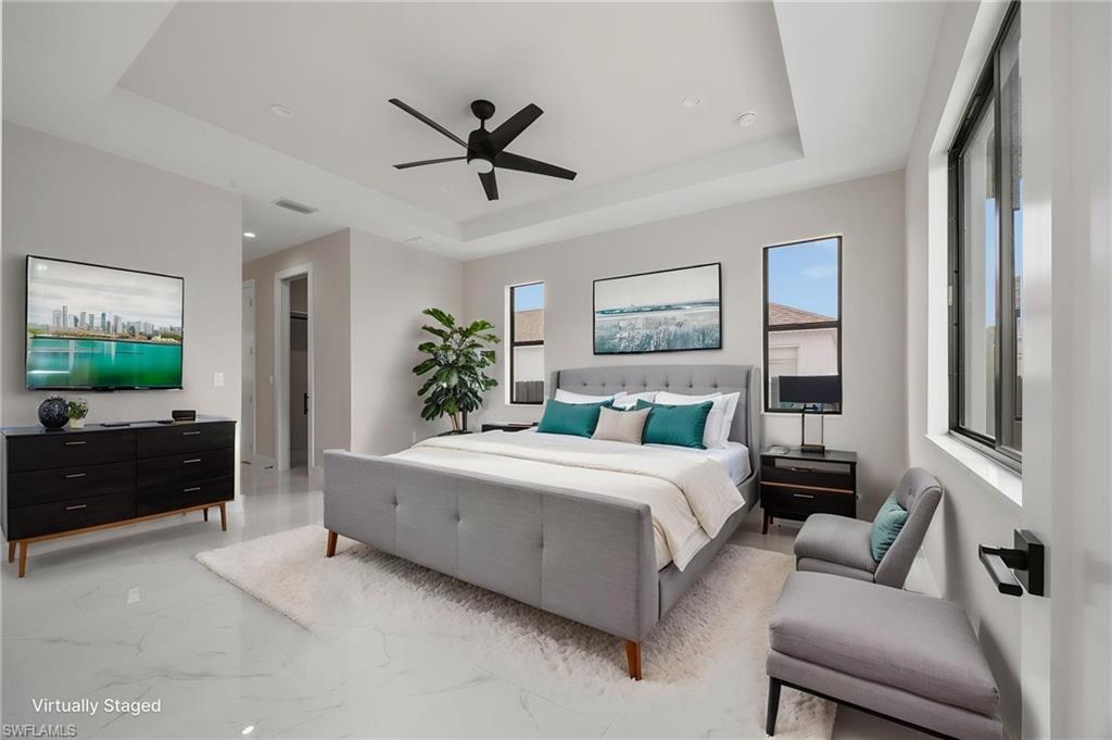 Bedroom with a ceiling fan, multiple windows, a tray ceiling, and light marble finish flooring