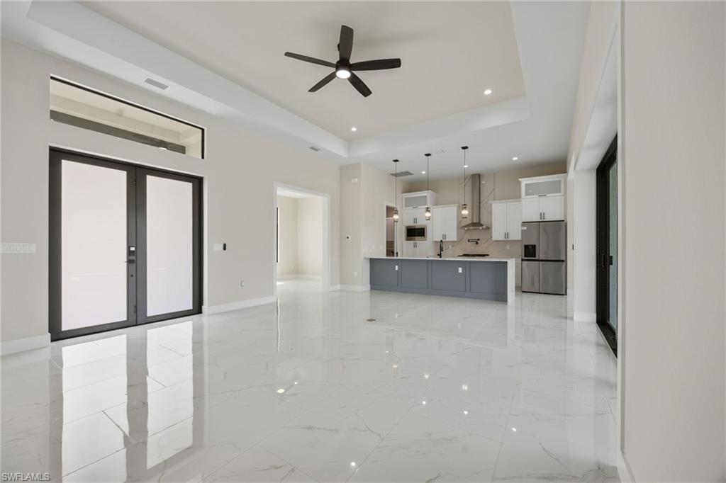Unfurnished living room with a ceiling fan, a raised ceiling, recessed lighting, french doors, and light marble finish floors