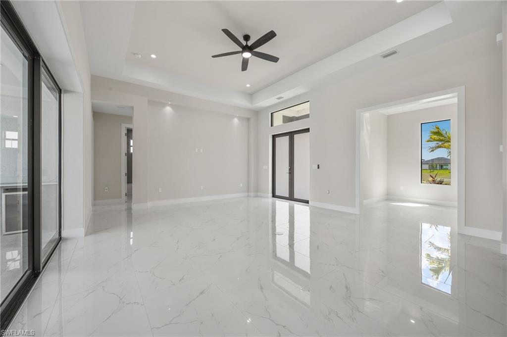 Empty room featuring french doors, a tray ceiling, a ceiling fan, recessed lighting, and light marble finish flooring