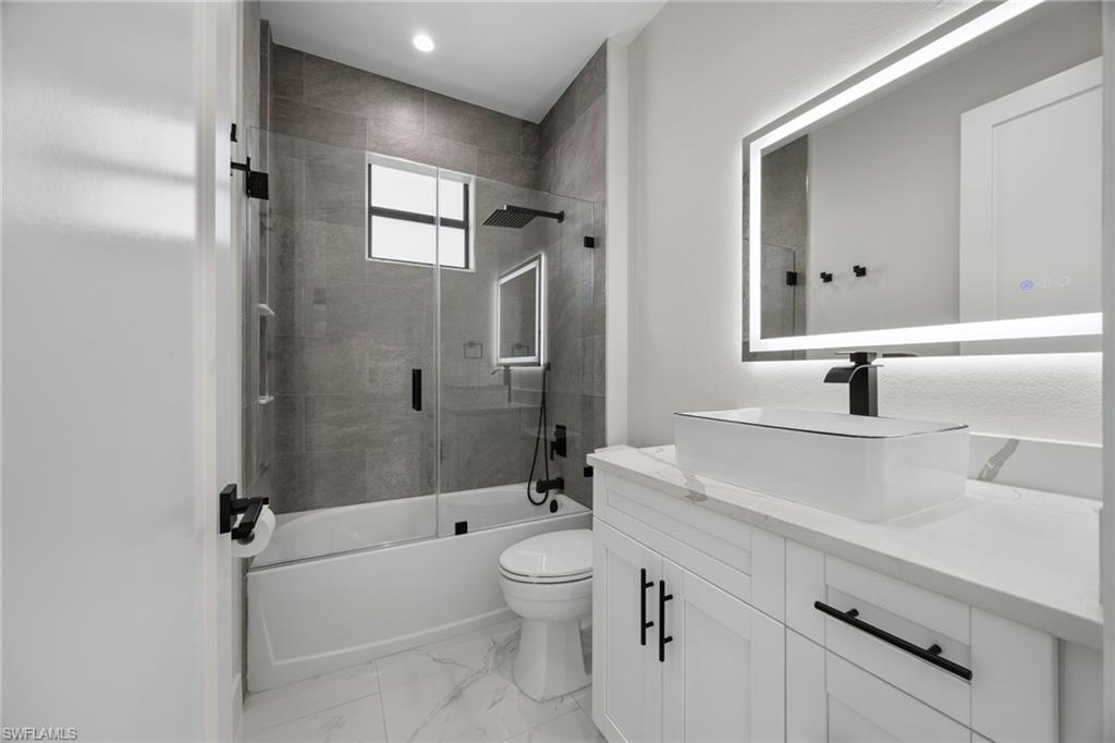 Bathroom featuring vanity, shower / bath combination with glass door, and light marble finish flooring