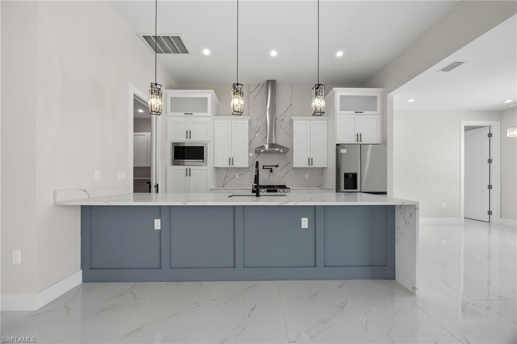 Kitchen featuring a peninsula, light stone counters, white cabinets, stainless steel appliances, and glass fronted cabinets