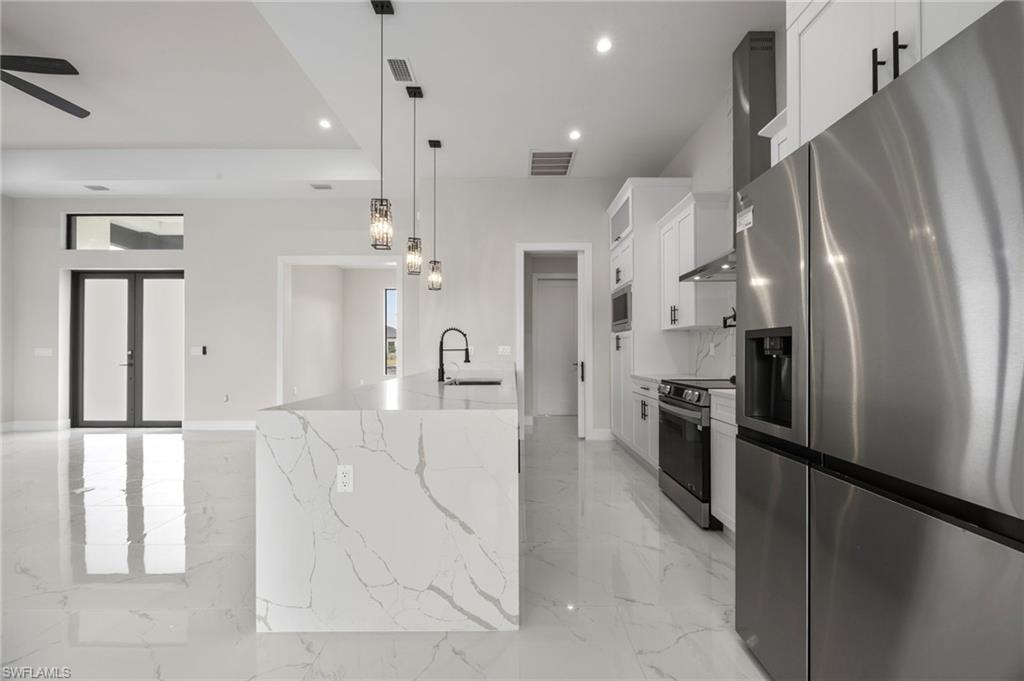 Kitchen featuring stainless steel appliances, white cabinets, light stone countertops, and light marble finish floors