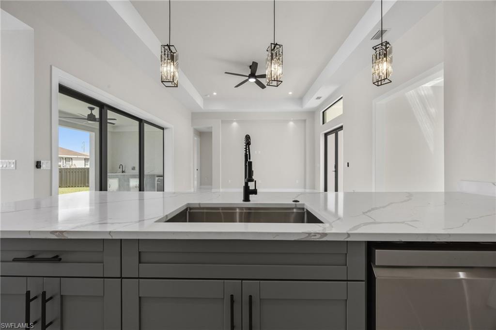Kitchen featuring light stone countertops, a tray ceiling, stainless steel dishwasher, ceiling fan, and gray cabinets