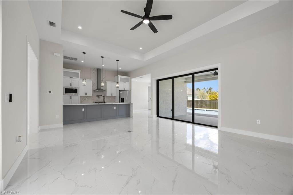 Unfurnished living room featuring a raised ceiling, recessed lighting, ceiling fan, and light marble finish floors