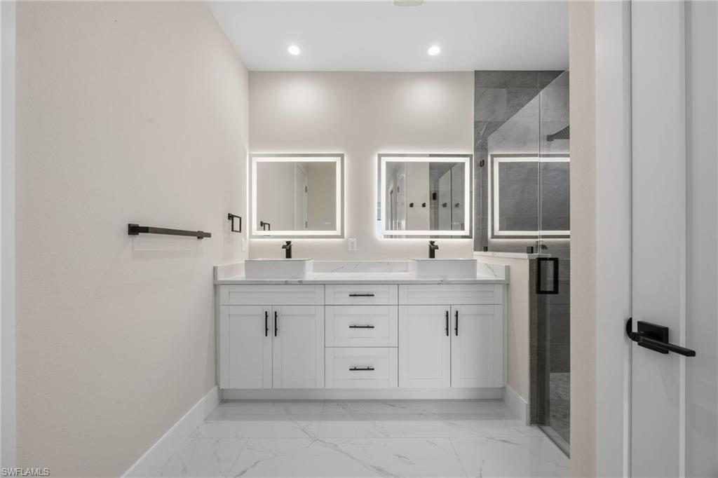 Bathroom featuring double vanity, a shower stall, recessed lighting, and light marble finish flooring