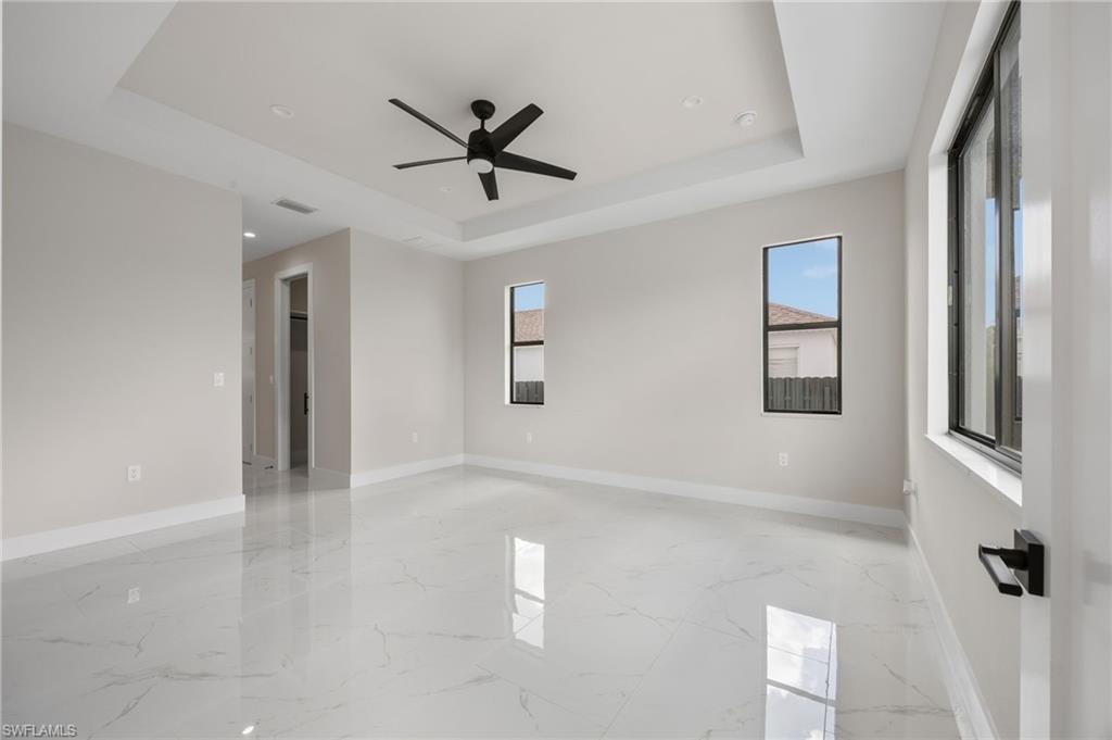 Empty room with ceiling fan, light marble finish floors, and a raised ceiling