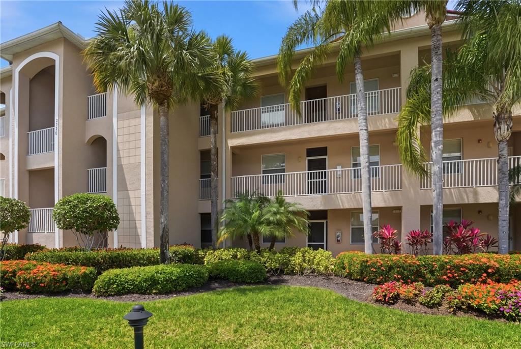 The property features a multi-story building with balconies, surrounded by lush landscaping, mature palm trees, and manicured lawns