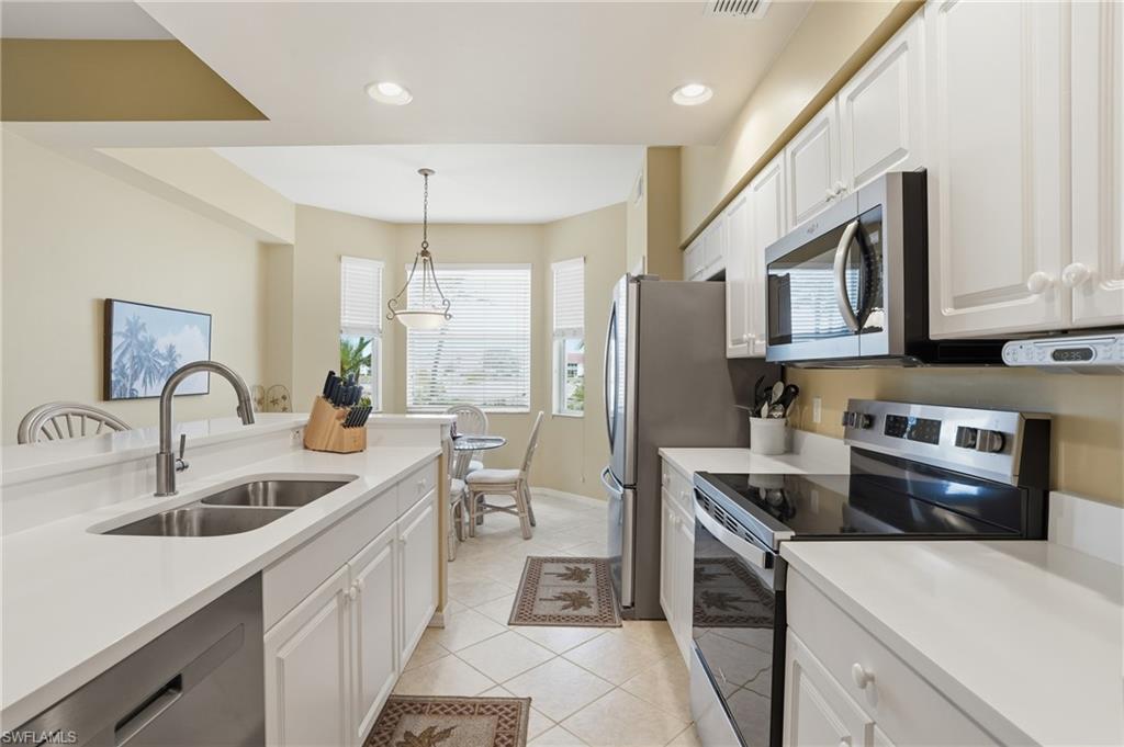Bright kitchen featuring white cabinetry, stainless steel appliances, a double basin sink, and tiled floors
