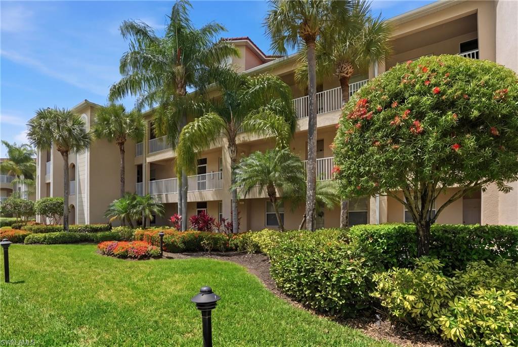 The property features well-maintained landscaping with green lawns, mature palm trees, and vibrant flowering shrubs
