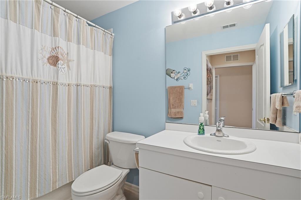 Bathroom featuring a vanity with a white countertop and an integrated sink, a large wall-mounted mirror, and a toilet
