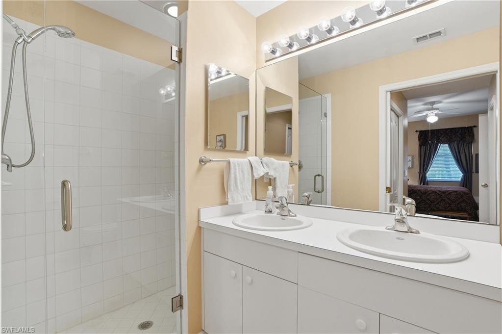 Well-appointed bathroom featuring a double vanity with two sinks, a large mirror with overhead lighting, and a glass-enclosed shower with white tiled walls