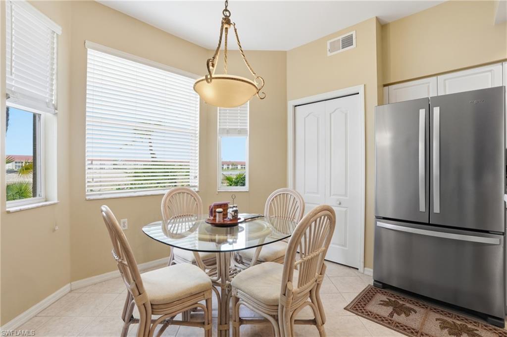 This dining area features abundant natural light from three windows, tiled flooring, and a contemporary stainless steel refrigerator