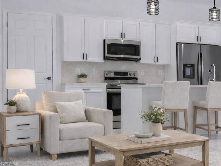Kitchen with stainless steel appliances, white cabinets, backsplash, light stone counters, and a kitchen breakfast bar