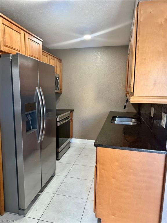 Kitchen featuring stainless steel appliances, light wood cabinetry, dark countertops, and tile flooring