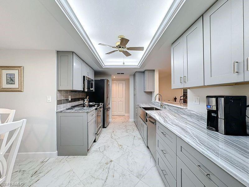 Kitchen with a raised ceiling, sink, gray cabinets, stainless steel appliances, and decorative backsplash