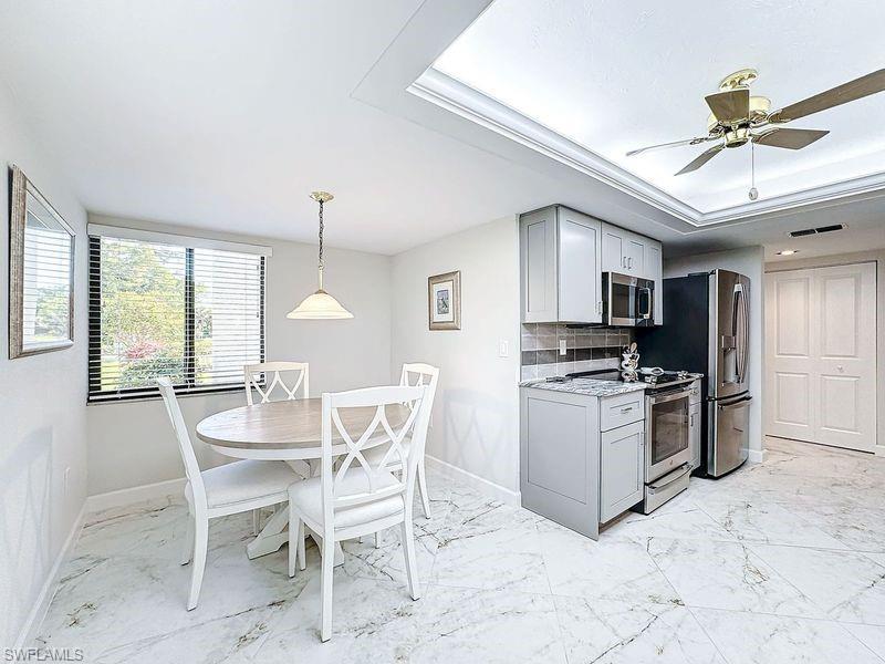 Kitchen featuring gray cabinets, light stone counters, decorative backsplash, appliances with stainless steel finishes, and ceiling fan