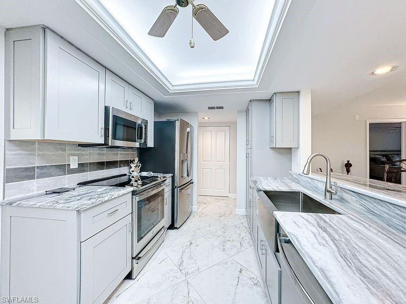 Kitchen with decorative backsplash, a tray ceiling, appliances with stainless steel finishes, and light stone countertops
