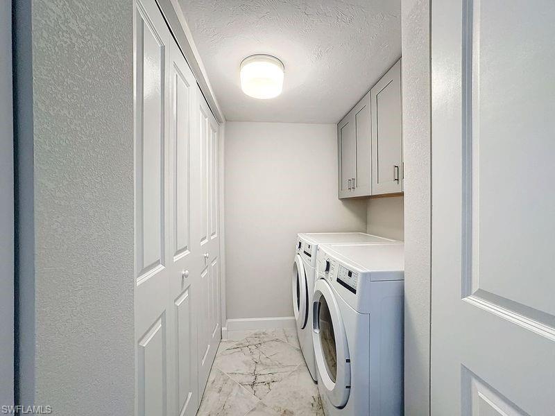 Laundry room with a textured ceiling, washing machine and dryer, and cabinets