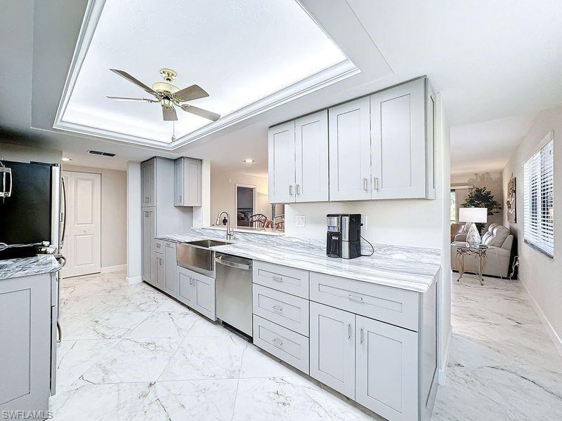 Kitchen with ceiling fan, sink, gray cabinetry, appliances with stainless steel finishes, and a tray ceiling