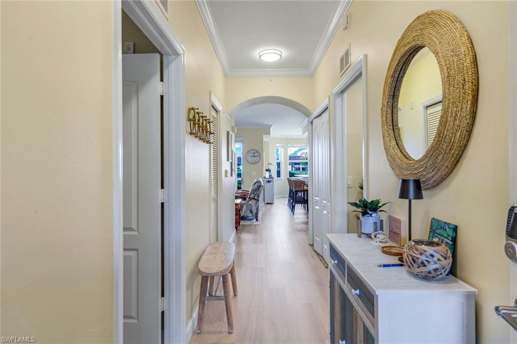 Hall with ornamental molding, light wood-type flooring, arched walkways, and visible vents