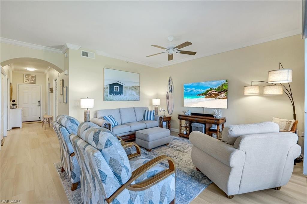 Living room with a ceiling fan, arched walkways, light wood finished floors, and visible vents