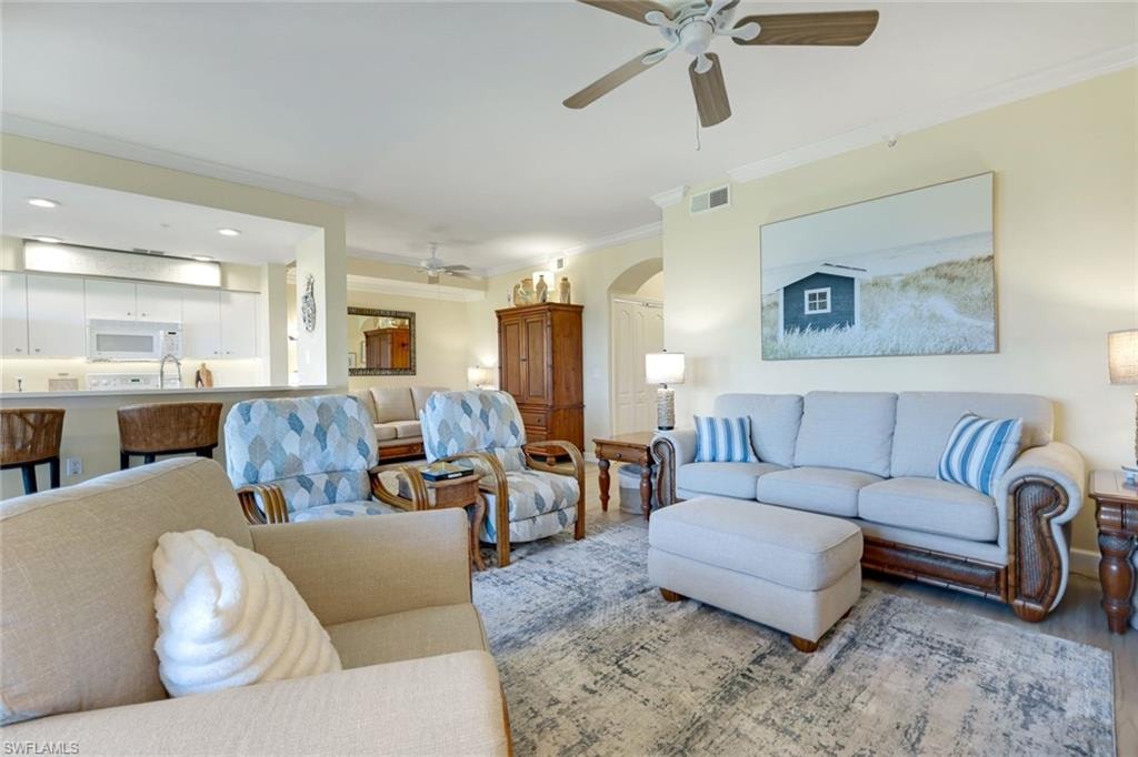 Living room with arched walkways, crown molding, and a ceiling fan