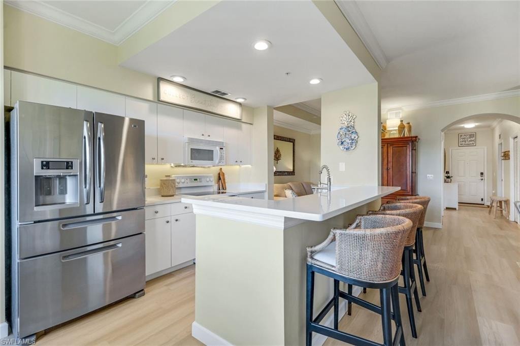 Kitchen with arched walkways, white microwave, stainless steel refrigerator with ice dispenser, and crown molding