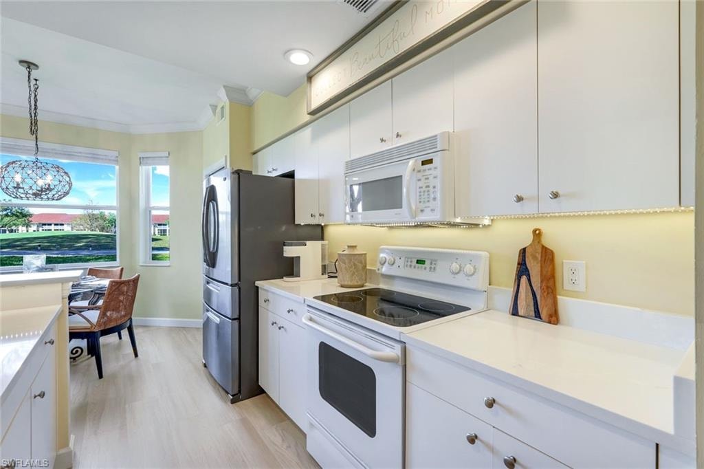 Kitchen with light countertops, crown molding, white appliances, white cabinetry, and decorative light fixtures