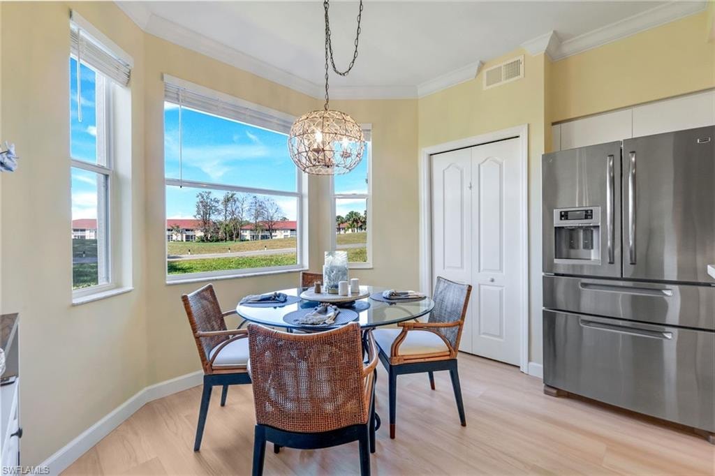 Dining space with a chandelier, baseboards, visible vents, light wood-style floors, and ornamental molding