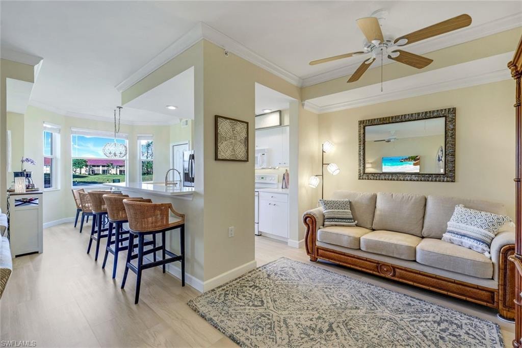 Living area with baseboards, light wood-type flooring, ornamental molding, and a ceiling fan
