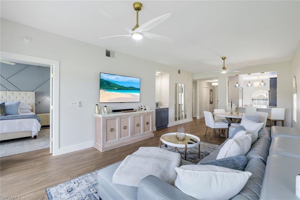 Living area featuring baseboards, visible vents, wood finished floors, and a ceiling fan
