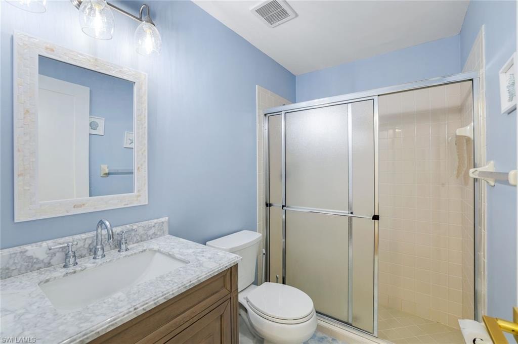 Full bathroom with a shower stall, visible vents, toilet, and vanity