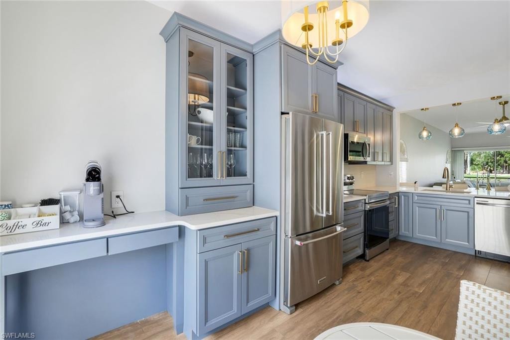 Kitchen featuring gray cabinets, a sink, appliances with stainless steel finishes, glass insert cabinets, and wood finished floors