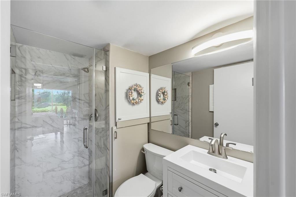 Bathroom featuring a frameless glass shower enclosure with marble-style tile, a white vanity with integrated sink, a brushed nickel faucet, a wall-mounted mirror, and an overhead vanity light