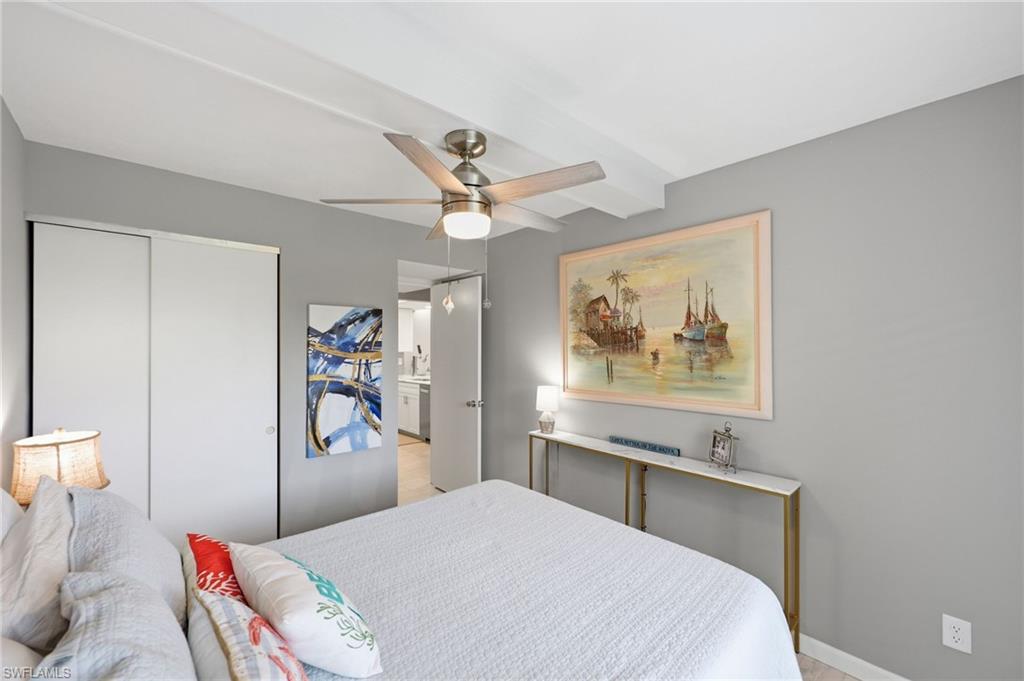 Bedroom featuring a ceiling fan with integrated lighting, exposed ceiling beams, and sliding closet doors