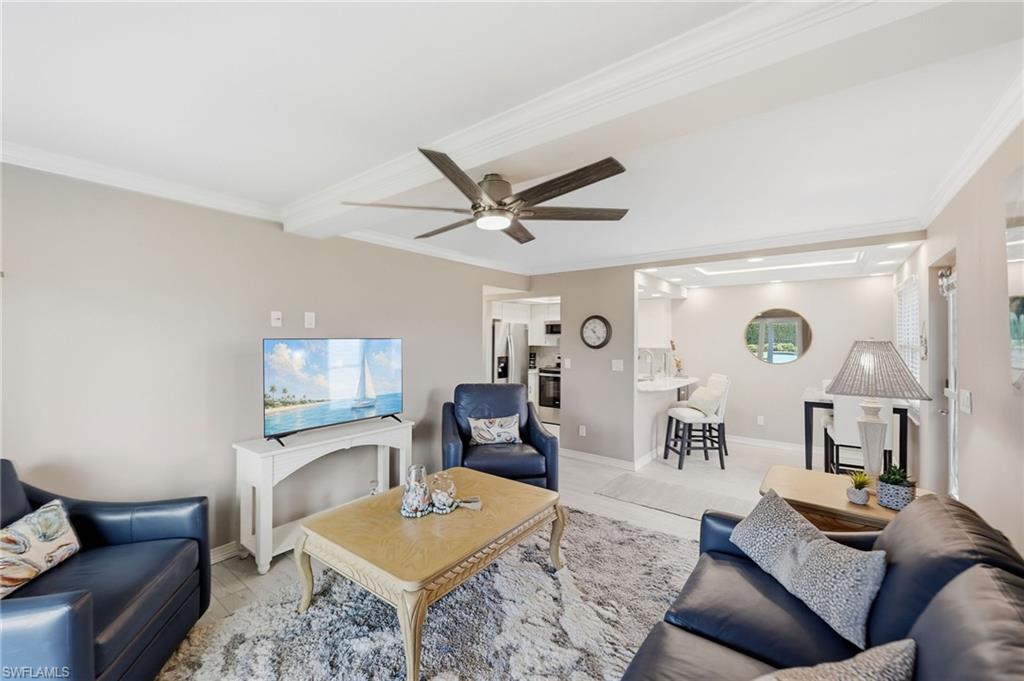 Open-concept living area featuring tray ceilings with crown molding, a ceiling fan with light fixture, tile flooring, and a breakfast bar with seating