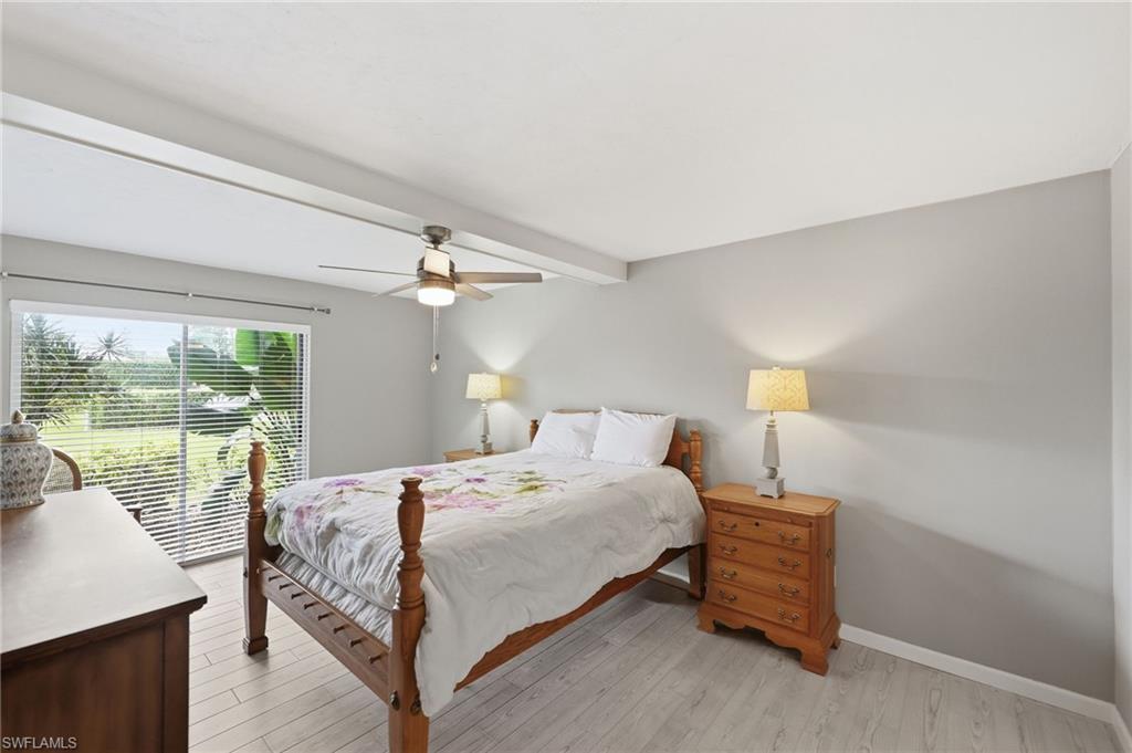 Bright room featuring a large sliding glass door with horizontal blinds, light wood-finish flooring, a ceiling fan with integrated lighting, and white exposed beam accents