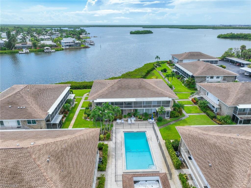 Waterfront community featuring multiple buildings with screened lanais, a central swimming pool with a surrounding patio, mature palm trees, and lush green landscaping