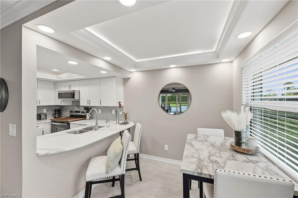 Bright kitchen and dining area featuring white cabinetry, stainless steel appliances, a breakfast bar, and recessed lighting