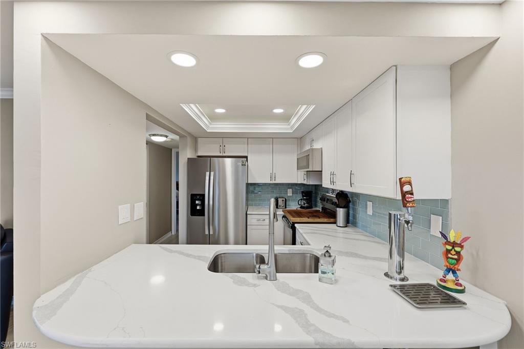 Kitchen featuring a large waterfall-edge countertop with integrated sink, stainless steel appliances, white cabinetry, and a blue subway tile backsplash