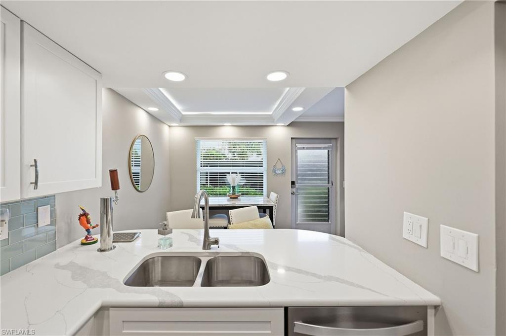 Kitchen featuring light cabinetry, a dual basin undermount sink, a gooseneck faucet, light-toned countertops with veining, and a tiled backsplash