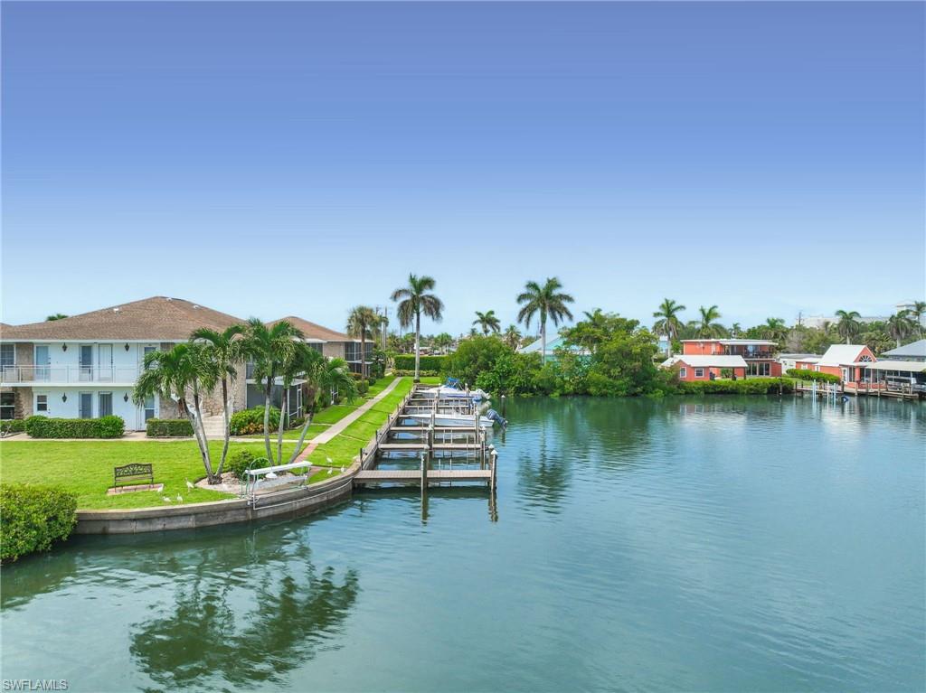 Waterfront property featuring multiple boat slips, a manicured lawn, and mature palm trees