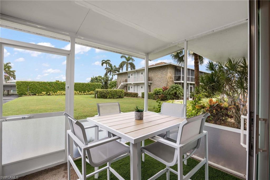 Screened lanai featuring a contemporary dining table with seating for four, framed by expansive glass panels overlooking manicured grounds